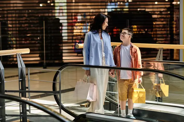 Una madre e suo figlio con la sindrome di Down condividono un sorriso mentre camminano lungo una scala mobile al centro commerciale, godendo del loro tempo insieme. — Foto stock