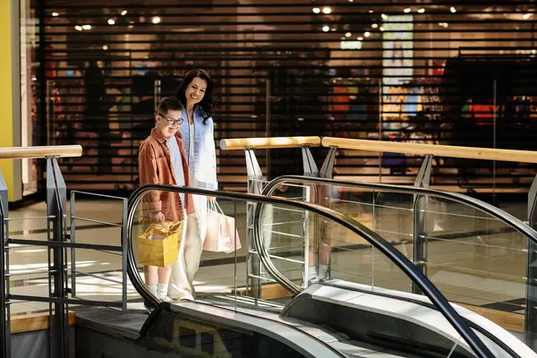 Una madre e suo figlio con la sindrome di Down stanno camminando su una scala mobile in un centro commerciale. — Foto stock