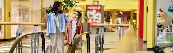 Мать и ее сын с синдромом Дауна наслаждаются прогулкой по торговому центру, улыбаясь, когда они идут вместе. — стоковое фото