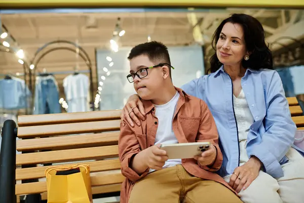 Eine Mutter und ihr Sohn mit Down-Syndrom sitzen auf einer Bank in einem Einkaufszentrum und genießen Gesellschaft. — Stockfoto