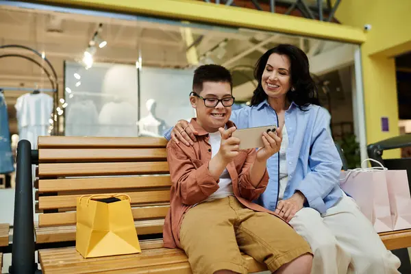 Eine Mutter und ihr Sohn mit Down-Syndrom lachen, während sie im Einkaufszentrum gemeinsam auf ein Telefon schauen. — Stockfoto