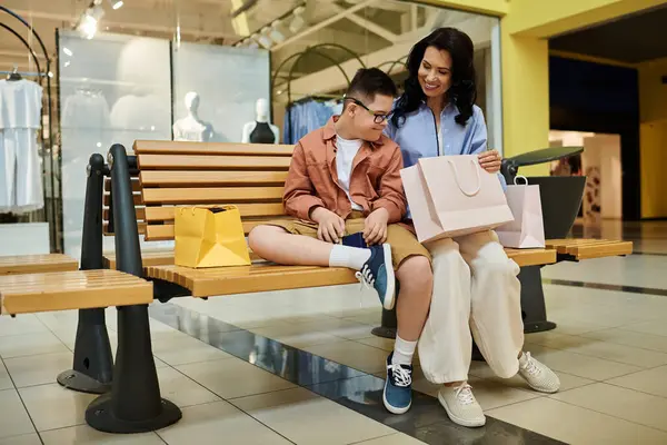 Une mère et son fils trisomique partagent un moment tendre sur un banc dans un centre commercial, leurs sourires reflétant un lien fort. — Photo de stock