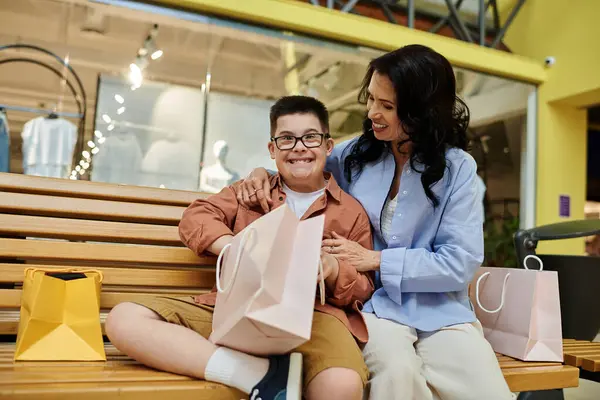 A mother and her son with Down syndrome are sitting on a bench in a shopping mall, enjoying a shopping spree together. — Stock Photo