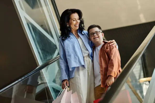Una madre e suo figlio con la sindrome di Down condividono un sorriso mentre camminano su una scala mobile in un centro commerciale.. — Foto stock