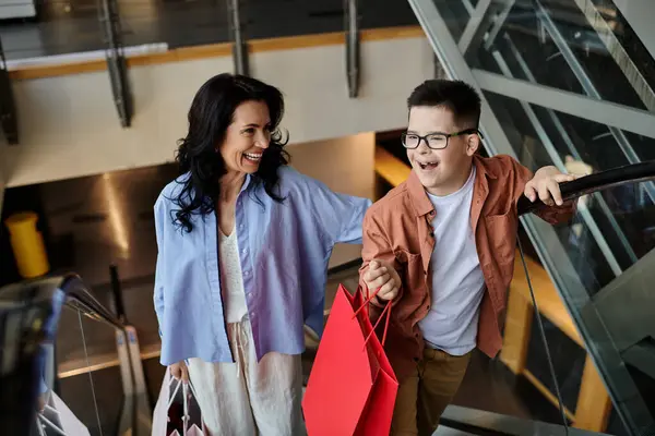 A mother and her son with Down syndrome share a happy moment while walking on an escalator in a shopping mall. — Stock Photo
