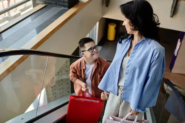 Una madre e suo figlio con la sindrome di Down camminano attraverso un centro commerciale, sorridendo e godendo il loro tempo insieme. — Foto stock