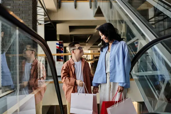 A mother and her son with Down syndrome share a lighthearted moment while shopping in a mall, both carrying bags and smiling at each other. — Stock Photo