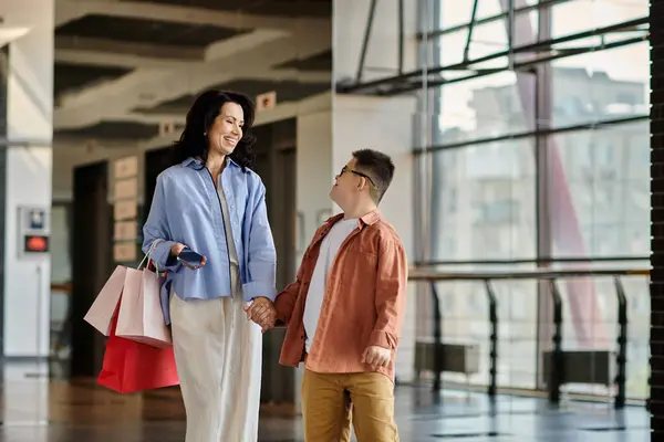 Uma mãe e seu filho com síndrome de Down compartilham um momento feliz enquanto caminham por um shopping, de mãos dadas. — Fotografia de Stock