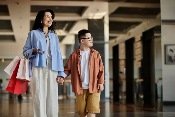 A mother and her son with Down syndrome walk hand-in-hand through a shopping mall, enjoying quality time together. — Stock Photo