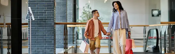 Una madre e suo figlio con la sindrome di Down camminano mano nella mano attraverso un centro commerciale, godendo di una giornata fuori insieme. — Foto stock