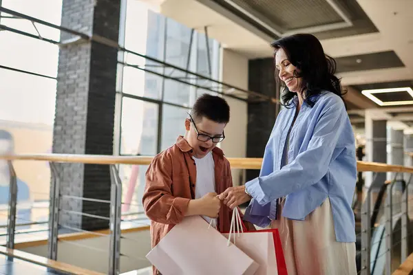 Une mère et son fils trisomique traversent un centre commercial, tenant des sacs à provisions. — Photo de stock