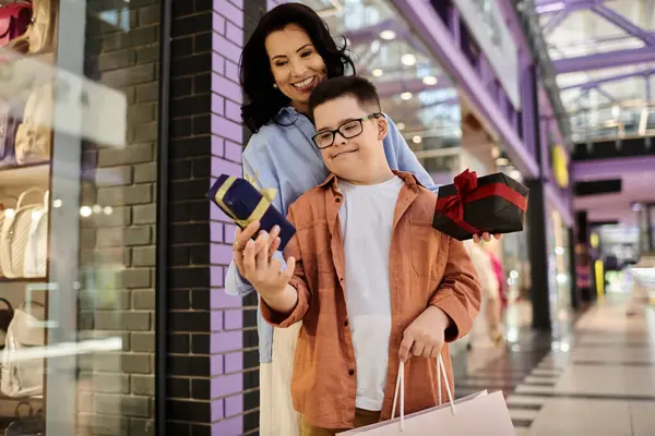 A mother and her son with Down syndrome walk through a shopping mall, holding gifts. — Stock Photo