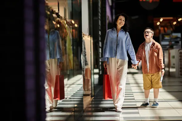 A mother and her son with Down syndrome walk hand-in-hand through a shopping mall, enjoying a day out together. — Stock Photo