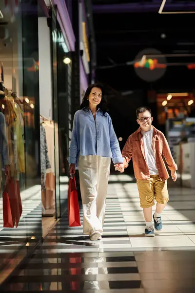 A mother and her son with Down syndrome walk hand-in-hand through a shopping mall, enjoying a day of shopping and bonding. — Stock Photo