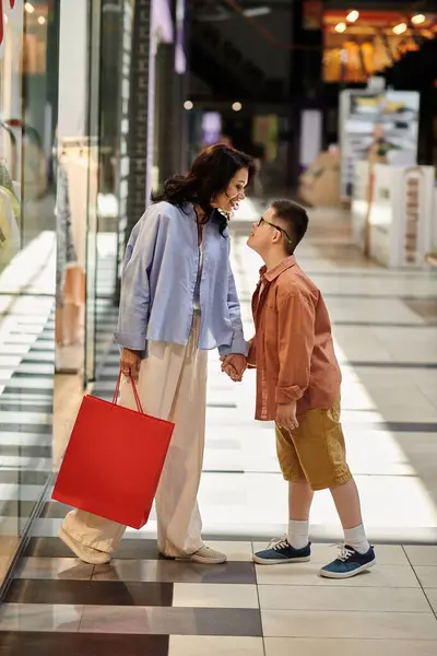 Una madre e suo figlio con la sindrome di Down camminano mano nella mano attraverso un centro commerciale.. — Foto stock