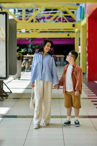 Une mère et son fils trisomique partagent un moment heureux en marchant dans un centre commercial. — Photo de stock