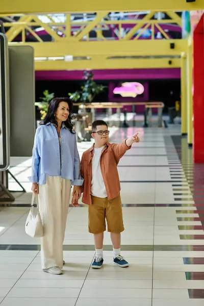 A mother and her son with Down syndrome walk hand-in-hand through a shopping mall, enjoying a fun day out together. — Stock Photo