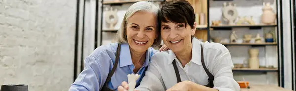 Two mature women, dressed in cozy attire, work on pottery in an art studio. — Stock Photo