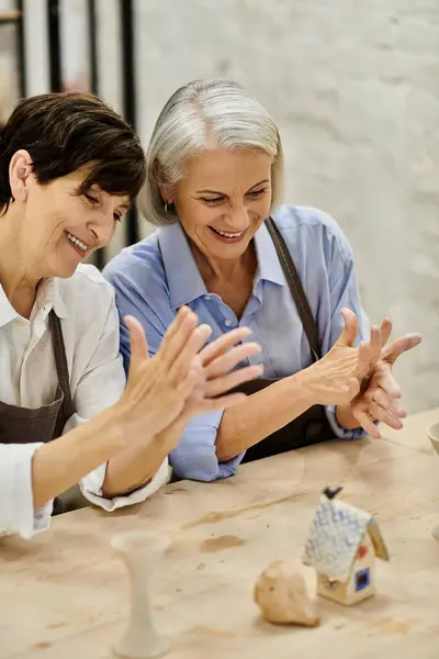 Two mature women, in cozy attire, are crafting together at an art studio, focusing on pottery. — Stock Photo