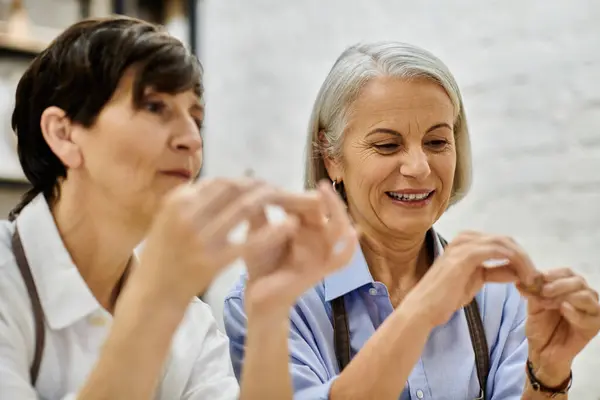 A mature lesbian couple, clad in cozy attire, crafts pottery together in a bright studio. — Stock Photo