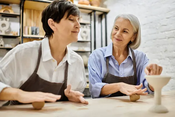 Two mature women, dressed in cozy attire, work with clay at a pottery studio. — Stock Photo