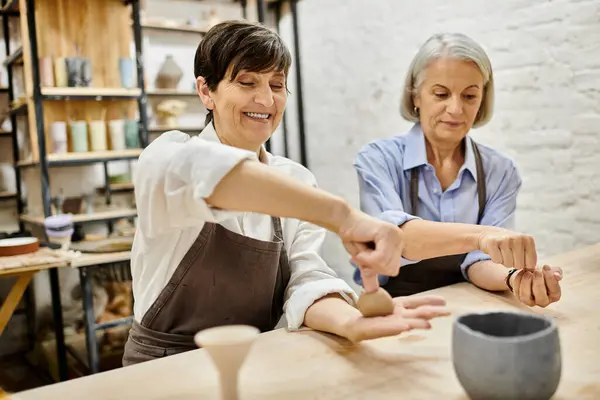 Two mature women, wearing aprons, work on pottery in a studio setting. — Stock Photo