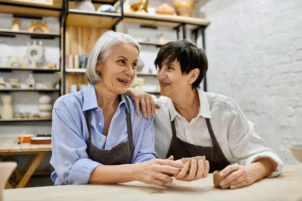 Two women, dressed in aprons, work together on a pottery project in a cozy studio setting. — Stock Photo