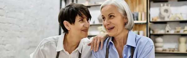 A mature lesbian couple, dressed in cozy attire, works on pottery projects in a well-lit studio. — Stock Photo