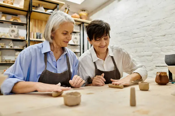 Two women, wearing aprons, work with clay at a pottery studio. — Stock Photo