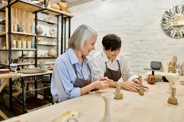 A senior lesbian couple works together on pottery in a light-filled studio. — Stock Photo