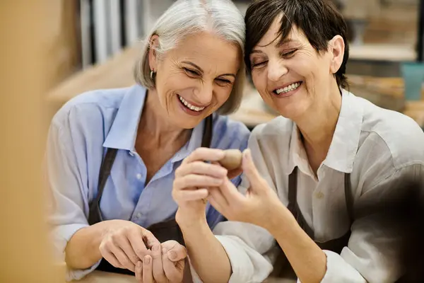 Two women in a pottery studio, laughing and looking at a clay creation. — Stock Photo