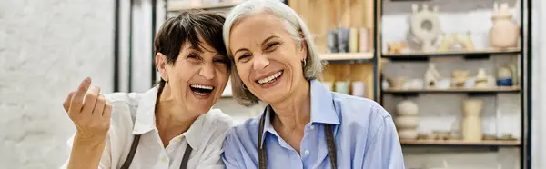 Two women, likely a couple, laugh together in a pottery studio, surrounded by their creations. — Stock Photo