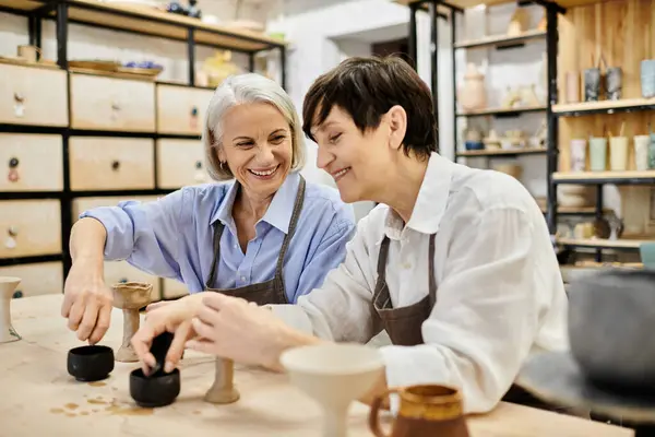 A mature lesbian couple smiles while crafting pottery in a cozy studio. — Stock Photo