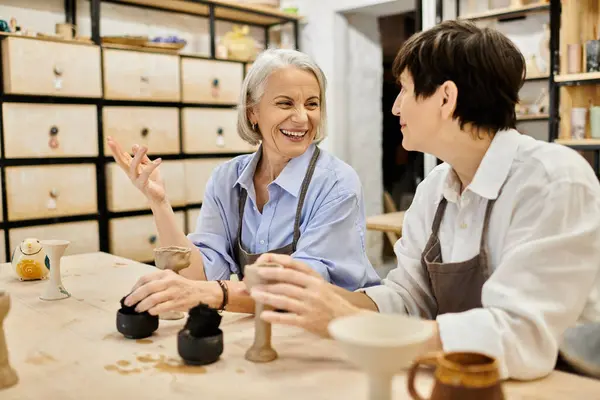 Two mature women in a pottery studio, working on clay projects and sharing a laugh. — Stock Photo