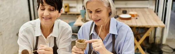 Two mature women in cozy attire work on pottery in an art studio. — Stock Photo
