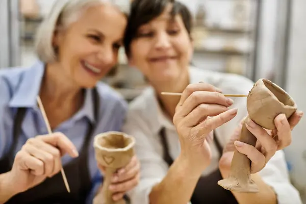 A mature lesbian couple smiles while crafting pottery in an art studio. — Stock Photo