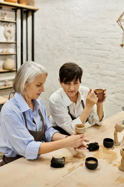 Two mature lesbians craft pottery together in cozy studio. — Stock Photo