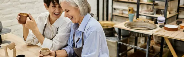 A mature lesbian couple laughs together while crafting pottery in an art studio. — Stock Photo