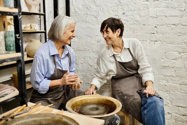 Two women in a pottery studio, one working on a clay piece. — Stock Photo