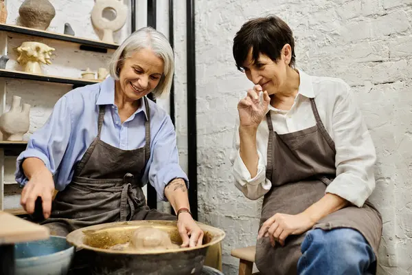 Two mature women wearing aprons work on pottery in a cozy studio. — Stock Photo