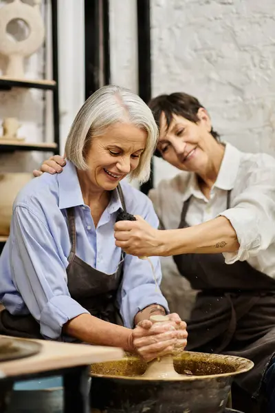 A mature lesbian couple, dressed in cozy attire, enjoy a pottery crafting session in a studio. — Stock Photo
