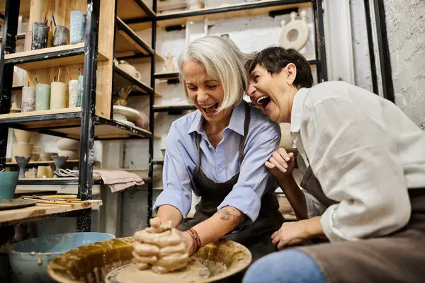 A lesbian couple enjoys pottery class, laughing as one shapes clay on a wheel. — Stock Photo
