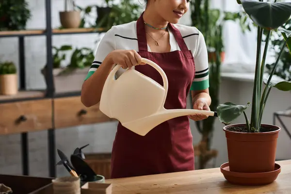 Cropped woman wearing an apron waters a plant in her plant shop. — Stock Photo