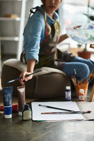 A young woman artist sits in her workshop, focused on her painting. — Stock Photo