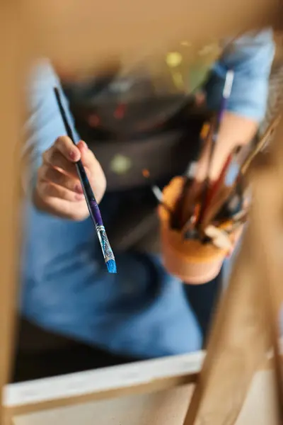 Молодая женщина в фартуке держит кисть, готовую к созданию в своей художественной студии. — стоковое фото