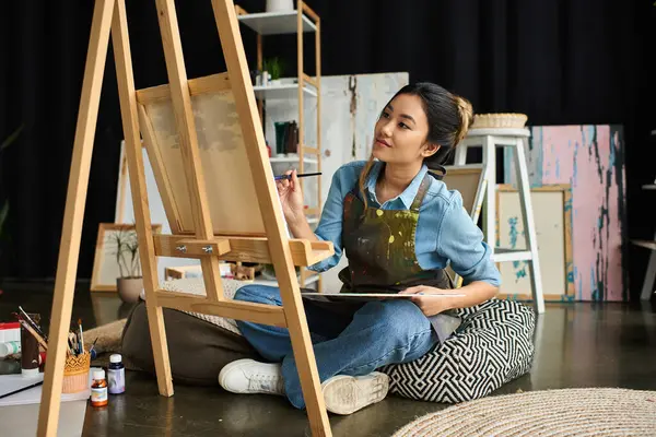 Una joven asiática en un delantal pinta sobre un lienzo en su taller. — Stock Photo