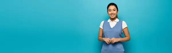 Eine junge Asiatin lächelt in blauer Weste und weißem Hemd vor hellblauem Hintergrund. — Stockfoto