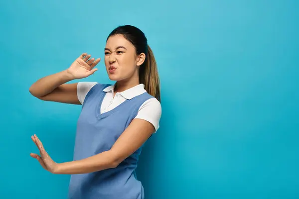 Une jeune femme asiatique en tenue décontractée chic se dresse sur un fond bleu, son expression suggérant un mélange de dégoût et d'incrédulité. — Photo de stock