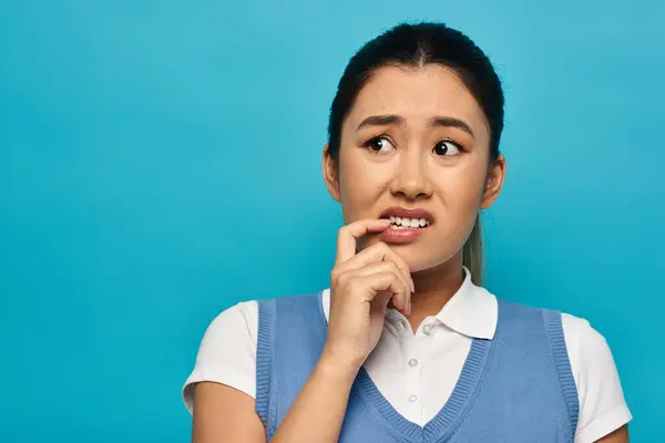 Una giovane donna asiatica in abbigliamento casual intelligente guarda pensieroso di lato, mordendosi il labbro mentre considera le sue opzioni. — Foto stock