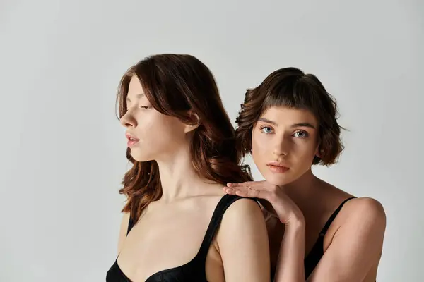 Two young women in black bodysuits pose against a gray backdrop, showcasing their love and connection. — Stock Photo